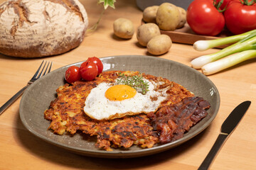 Rösti Teller mit Ei undSpeck auf Holztisch und Gemüse.