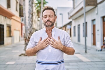 Middle age man outdoor at the city smiling with hands on chest with closed eyes and grateful...