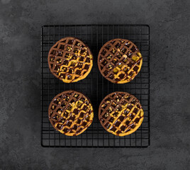 Round Viennese cocoa pumpkin waffles with chocolate sauce and walnuts on a metal stand on a dark gray background top view