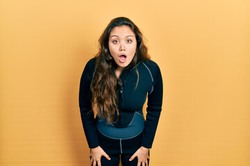 Young hispanic girl wearing diver neoprene uniform afraid and shocked with surprise and amazed...