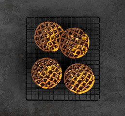 Viennese pumpkin chocolate waffles with sauce and walnuts on a metal stand on a dark gray background top view
