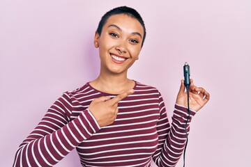 Beautiful hispanic woman with short hair holding usb charger adapter for the car smiling happy pointing with hand and finger