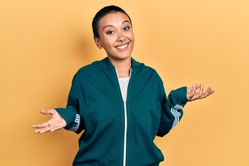 Beautiful hispanic woman with short hair wearing sporty jacket clueless and confused expression...