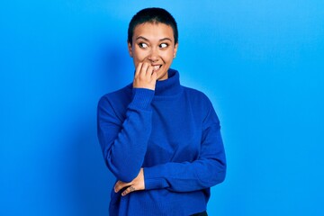 Beautiful hispanic woman with short hair wearing turtleneck sweater looking stressed and nervous with hands on mouth biting nails. anxiety problem.