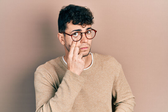 Young hispanic man wearing casual clothes and glasses pointing to the eye watching you gesture, suspicious expression
