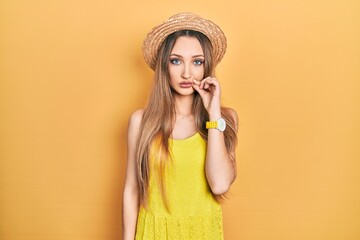 Young blonde girl wearing summer hat mouth and lips shut as zip with fingers. secret and silent,...