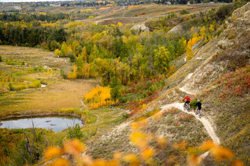 Two mountain bikers ride the Bowmont trail system in autumn colours above Dale Hodges Park in Calgary Alberta Canada