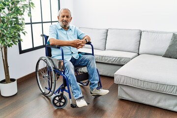Handsome senior man sitting on wheelchair at the living room with a happy and cool smile on face....