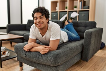 Young hispanic man smiling happy lying on the sofa at home.