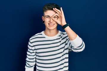 Naklejka premium Young caucasian boy with ears dilation wearing casual striped shirt doing ok gesture with hand smiling, eye looking through fingers with happy face.
