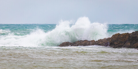 A large wave splashes over a spit of rock