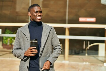 Young african american man smiling happy drinking coffee at the city