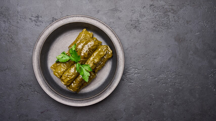 Panoramic view traditional Middle Eastern dish dolma, stuffed grape leaves and parsley in black plate on dark wood background. Flat lay. Copy space