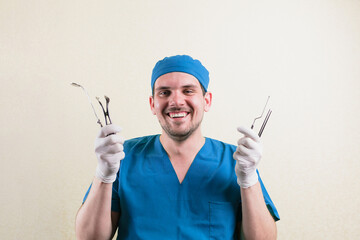 Young smiling doctor with medical instruments in his hand in blue surgeon suit isolated