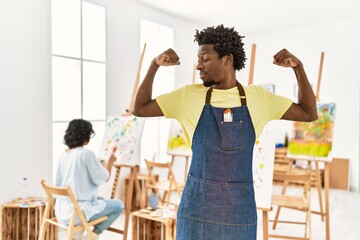 African young man standing at art studio showing arms muscles smiling proud. fitness concept.