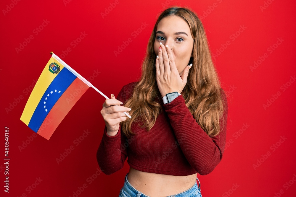 Sticker young blonde woman holding venezuelan flag covering mouth with hand, shocked and afraid for mistake.