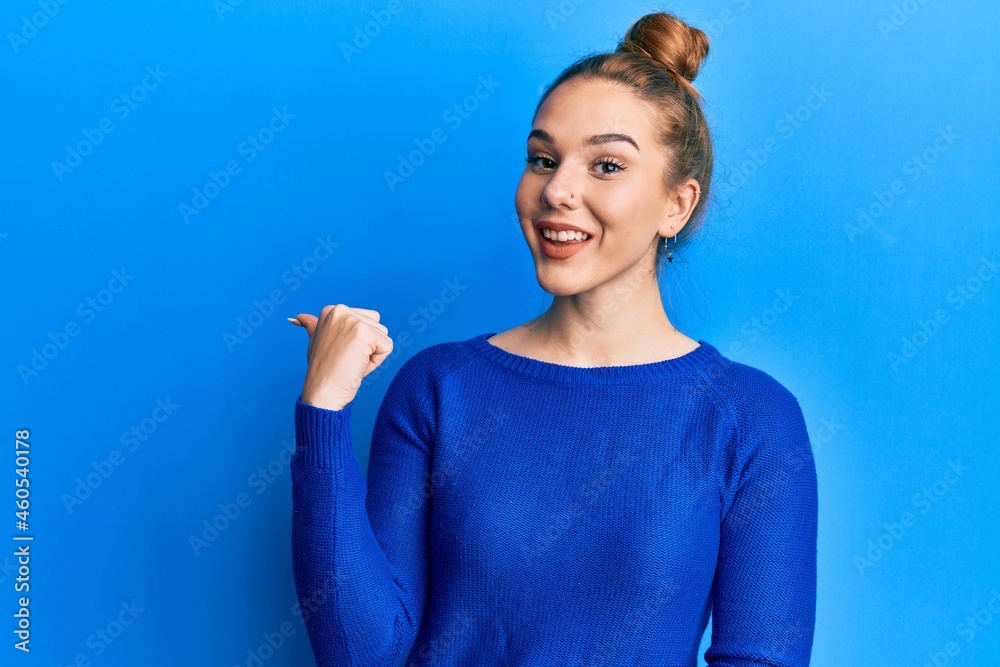 Poster Young blonde woman wearing casual clothes pointing thumb up to the side smiling happy with open mouth