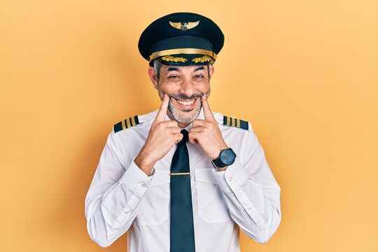 Handsome middle age man with grey hair wearing airplane pilot uniform smiling with open mouth, fingers pointing and forcing cheerful smile