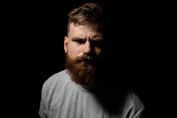 Obraz premium Close-up portrait of a handsome a brunette brutal bearded man in a grey t-shirt. Stylish and handsome man with a beard.
