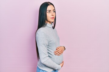 Fototapeta premium Beautiful woman with blue eyes expecting a baby, touching pregnant belly looking to side, relax profile pose with natural face and confident smile.