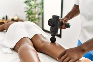 African american woman reciving legs massage with gun percusion at beauty center.