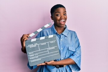 Young african american woman holding video film clapboard winking looking at the camera with sexy...