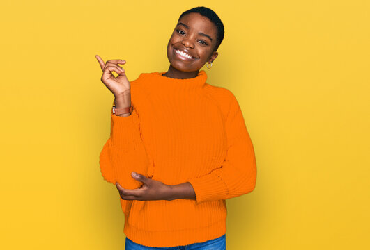 Young african american woman wearing casual clothes with a big smile on face, pointing with hand and finger to the side looking at the camera.