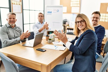 Group of middle age business workers smiling happy. Sitting on the table clapping and looking to the camera at the office.