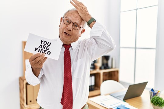 Senior business man holding you are fired banner at the office stressed and frustrated with hand on head, surprised and angry face