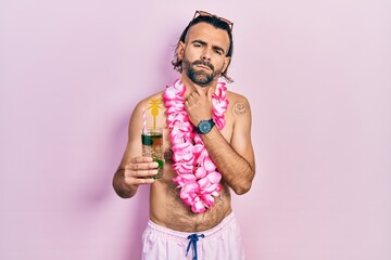 Young hispanic man wearing swimsuit and hawaiian lei drinking tropical cocktail touching painful neck, sore throat for flu, clod and infection