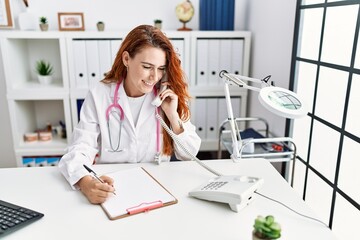 Fototapeta na wymiar Young redhead woman wearing doctor uniform talking on the telephone at hospital