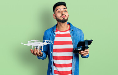 Young hispanic man with beard using drone with remote control looking at the camera blowing a kiss being lovely and sexy. love expression.