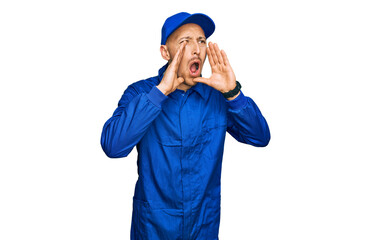 Bald man with beard wearing builder jumpsuit uniform shouting angry out loud with hands over mouth