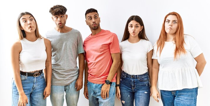 Group of young friends standing together over isolated background making fish face with lips, crazy and comical gesture. funny expression.