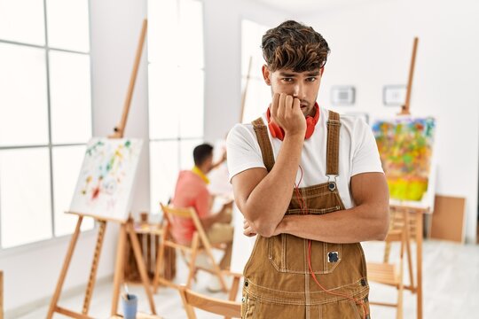 Young hispanic man at art studio looking stressed and nervous with hands on mouth biting nails. anxiety problem.