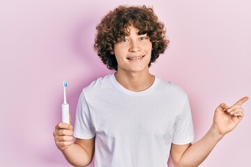 Handsome young man holding electric toothbrush smiling happy pointing with hand and finger to the...