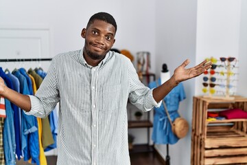 Young african american man working as manager at retail boutique clueless and confused expression...