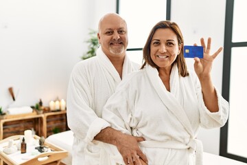 Middle age hispanic couple smiling happy and  holding credit card at beauty center.