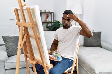 Young african man painting on canvas at home worried and stressed about a problem with hand on forehead, nervous and anxious for crisis