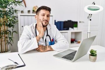 Young doctor working at the clinic using computer laptop touching mouth with hand with painful expression because of toothache or dental illness on teeth. dentist