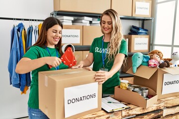 Two young volunteers woman smiling happy packing donations box at charity center.