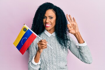 Middle age african american woman holding venezuelan flag doing ok sign with fingers, smiling friendly gesturing excellent symbol