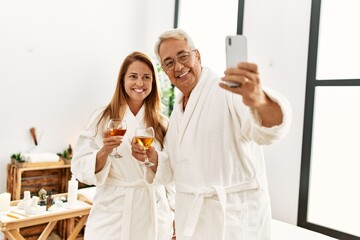 Fototapeta na wymiar Middle age hispanic couple drinking champagne make selfie by the smartphone at wellness center.