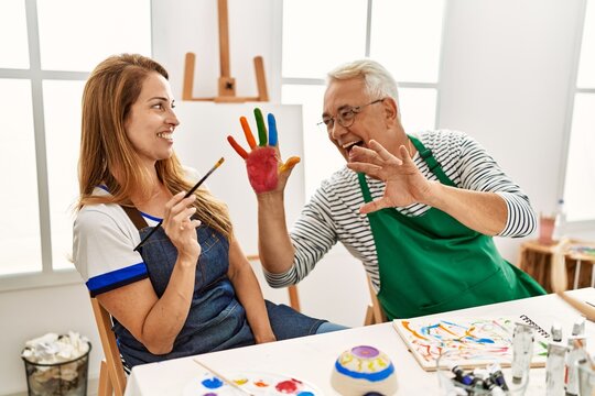 Two middle age artists smiling happy and showing painted hands at art studio.