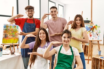 Group of five hispanic artists at art studio gesturing with hands showing big and large size sign, measure symbol. smiling looking at the camera. measuring concept.
