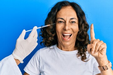 Middle age hispanic woman getting beauty treatment smiling with an idea or question pointing finger...