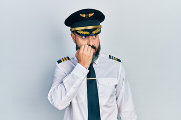 Young hispanic man wearing airplane pilot uniform looking stressed and nervous with hands on mouth biting nails. anxiety problem.