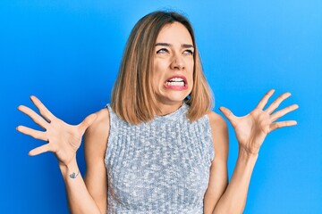 Young caucasian blonde woman wearing casual t shirt crazy and mad shouting and yelling with...