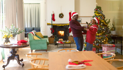 Happy african american senior couple in santa hats dancing at home at christmas time