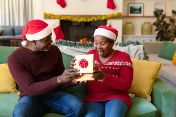 Surprised african american senior couple in santa hats sharing presents at christmas time